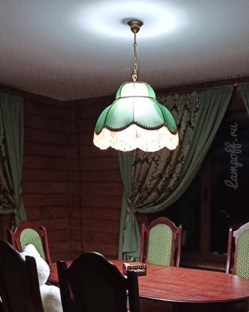 Зеленый абажур с бахромой над столом