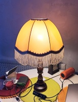 Включенная ретро лампа с бахромой на столике.